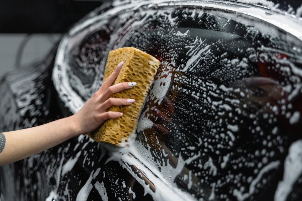 Mastering the First Impression: Your intriguing post title goes here A hand scrubs a car window with a sponge, covered in soap and foam, at a car wash.